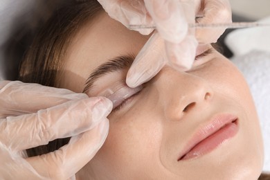 Photo of Eyelash lamination procedure. Esthetician placing silicone pad on woman's eyelid in beauty salon, closeup