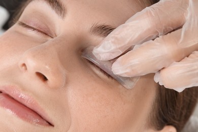 Photo of Eyelash lamination procedure. Esthetician placing silicone pad on woman's eyelid in beauty salon, closeup