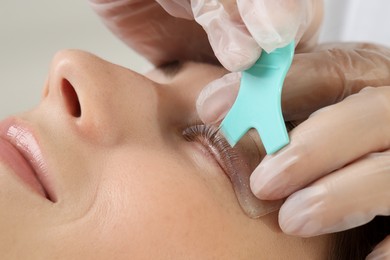 Photo of Eyelash lamination procedure. Esthetician applying adhesive on woman's lashes in beauty salon, closeup