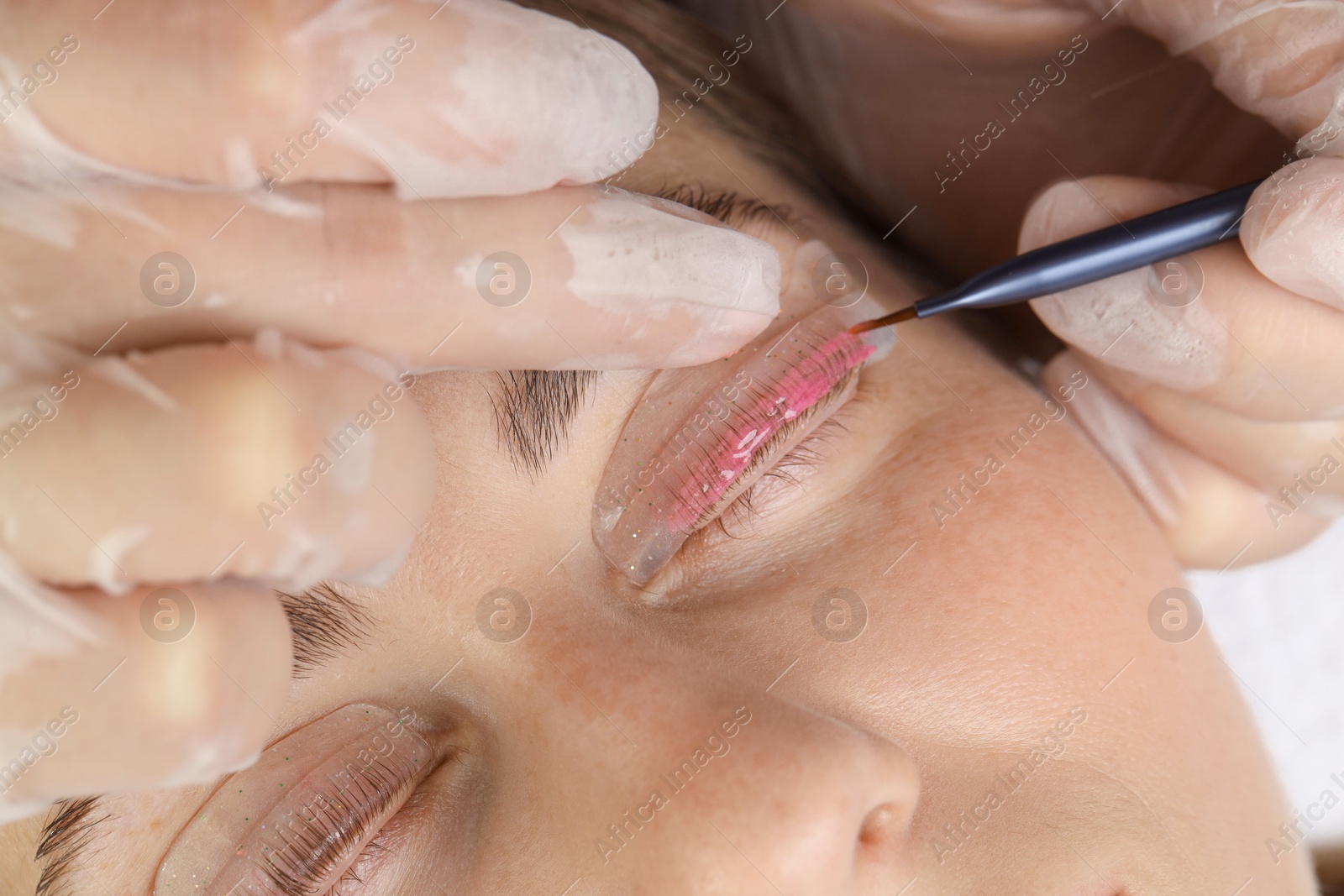 Photo of Eyelash lamination procedure. Esthetician applying lotion on woman's lashes in beauty salon, closeup