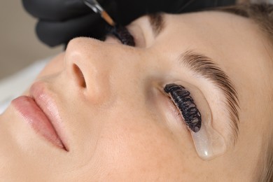 Photo of Eyelash lamination procedure. Esthetician applying dye on woman's eyelashes in beauty salon, closeup