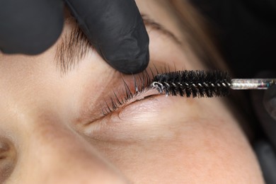 Photo of Esthetician brushing woman's lashes after lamination procedure, closeup