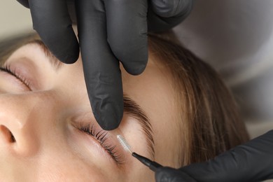 Photo of Esthetician brushing woman's lashes after lamination procedure, closeup