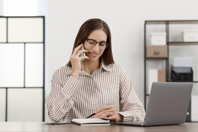 Photo of Banker talking on smartphone while working at table in office