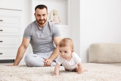 Photo of Father watching his little baby learning to crawl at home, selective focus