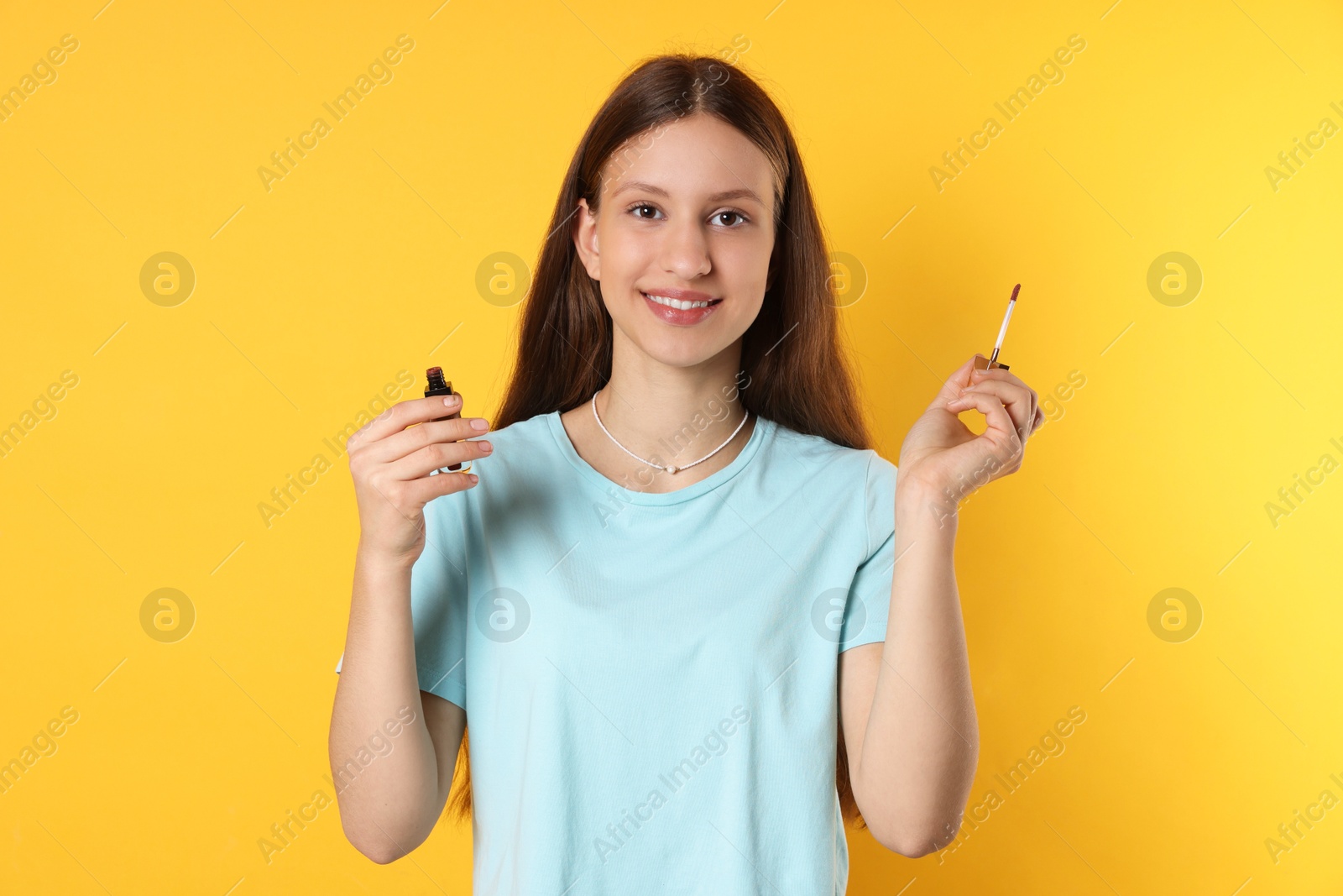 Photo of Smiling teenage girl with lip gloss on yellow background