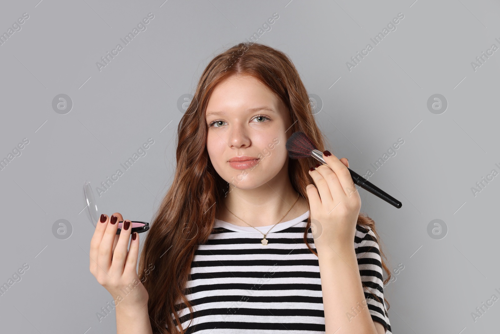 Photo of Teenage girl applying blusher with makeup brush on grey background