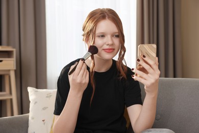 Teenage girl applying blusher with makeup brush at home