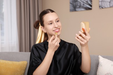 Photo of Smiling teenage girl applying lipstick at home