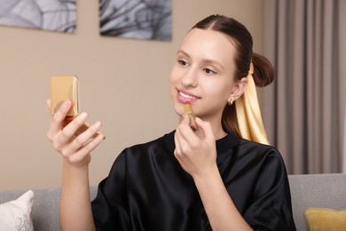 Photo of Smiling teenage girl applying lipstick at home