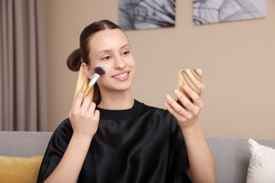 Photo of Smiling teenage girl applying blusher with makeup brush at home