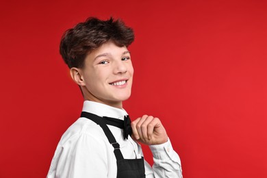 Photo of Teenage boy in apron and bowtie working as waiter on red background. Space for text