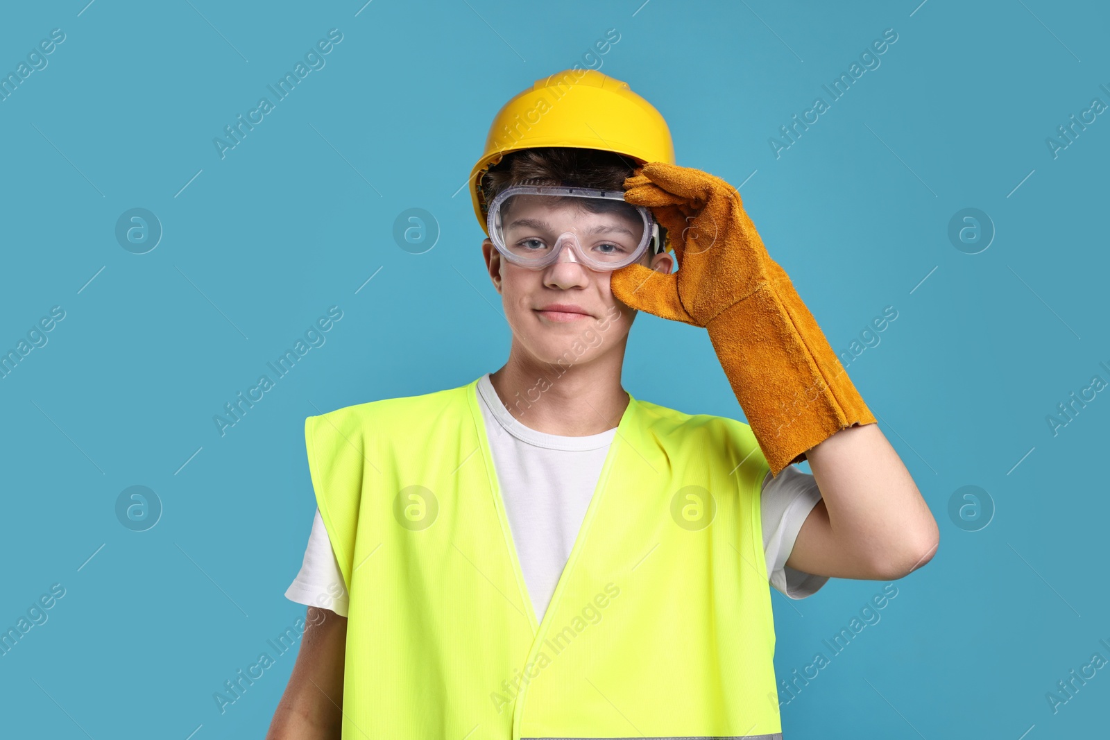 Photo of Teenage boy in hardhat, protective mask and safety vest working as builder on blue background