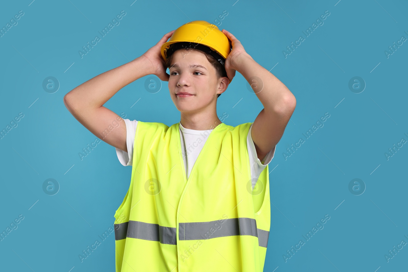 Photo of Teenage boy in hardhat and safety vest working as builder on blue background