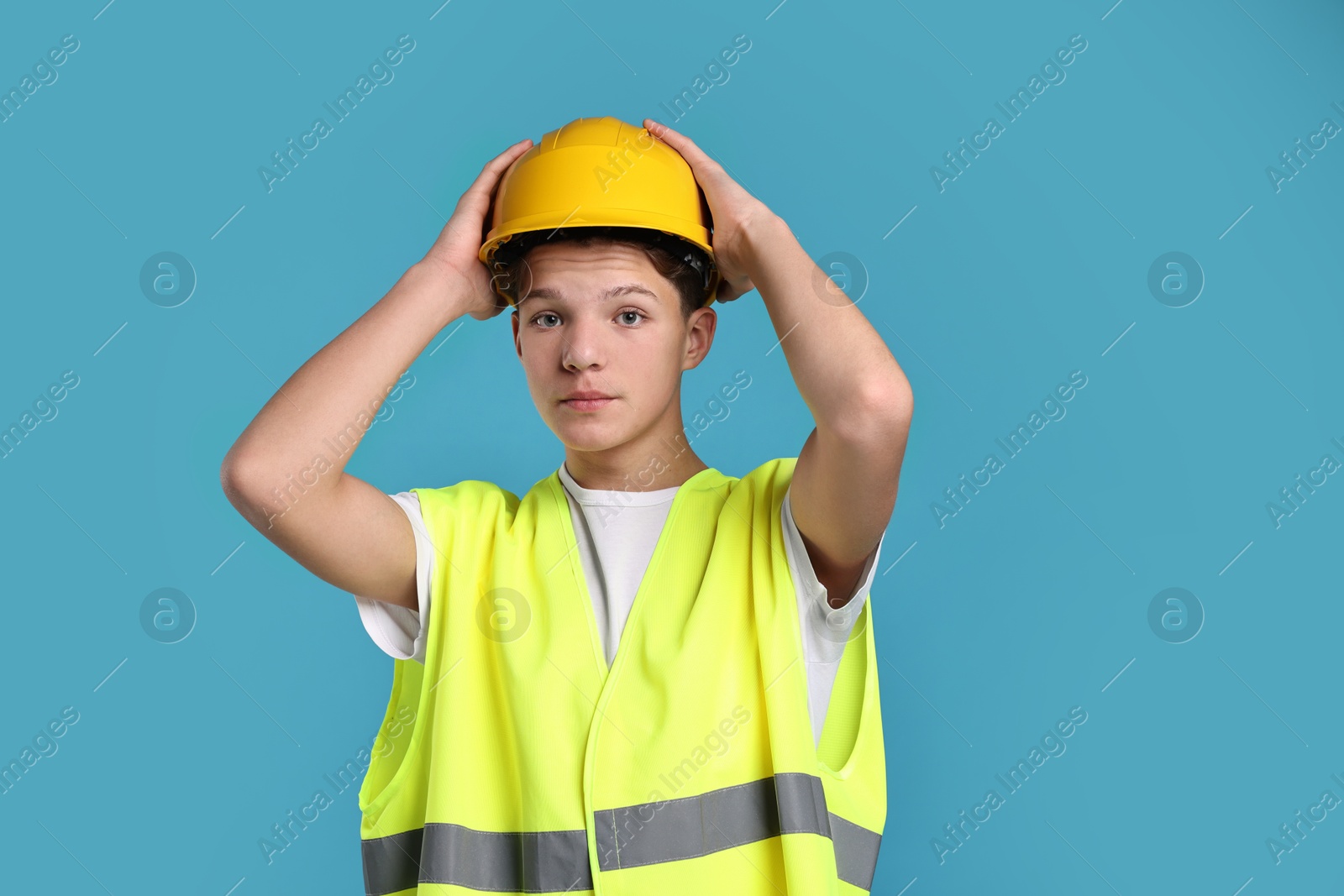 Photo of Teenage boy in hardhat and safety vest working as builder on blue background