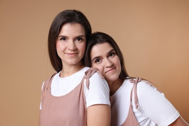 Portrait of beautiful twin sisters on pale brown background