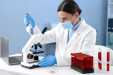 Photo of Laboratory testing. Doctor dripping blood sample onto glass slide while working with microscope at table indoors