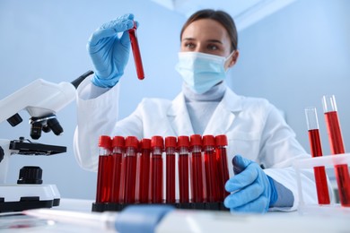 Photo of Laboratory testing. Doctor taking test tube with blood sample at table indoors, low angle view