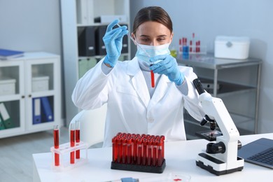 Laboratory testing. Doctor dripping blood sample into test tube at table indoors