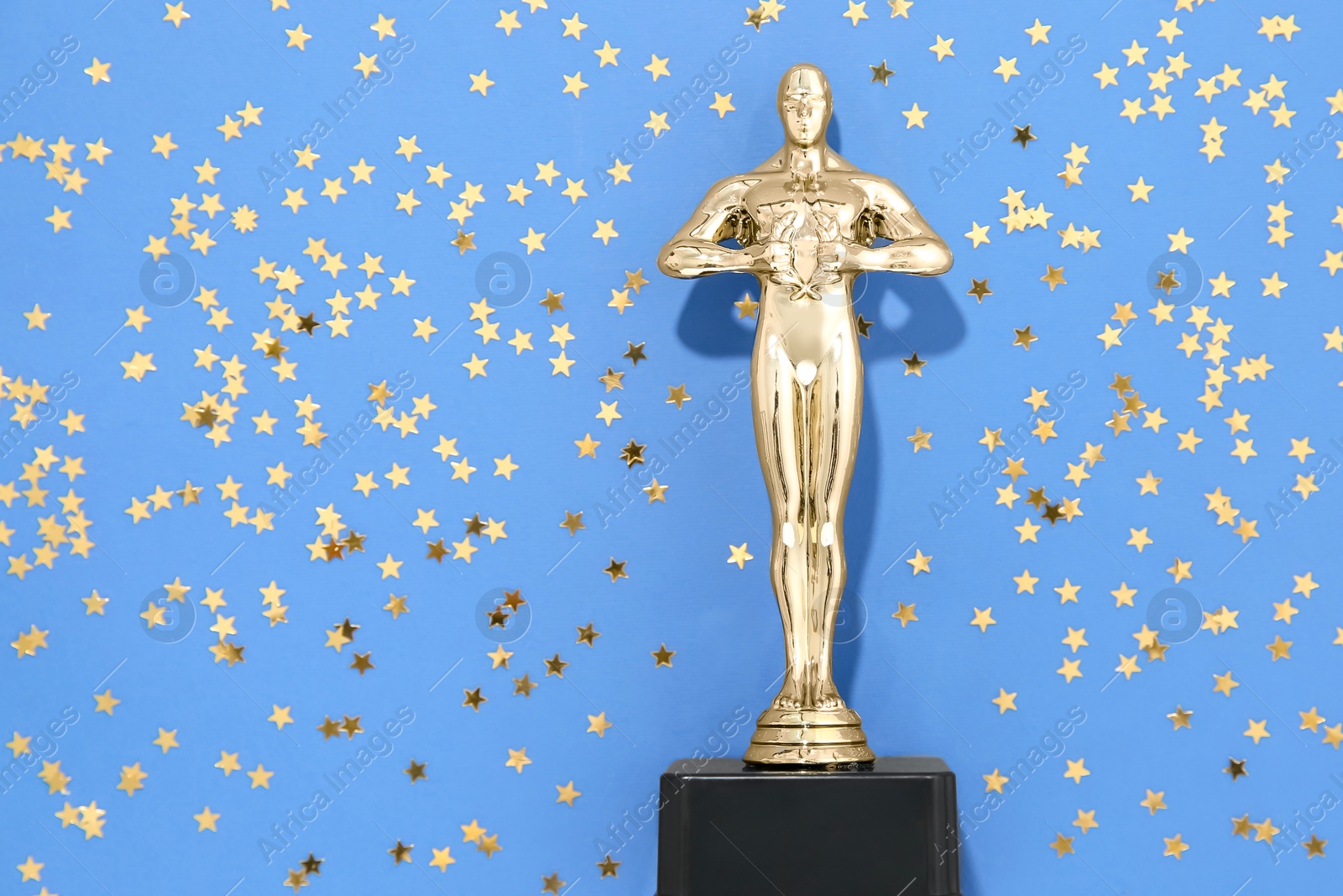 Photo of Golden trophy in shape of human figure and shiny confetti on light blue background, top view