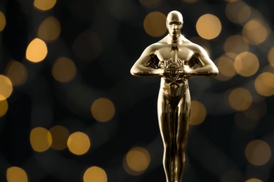 Photo of Golden trophy in shape of human figure on black background with blurred lights, space for text