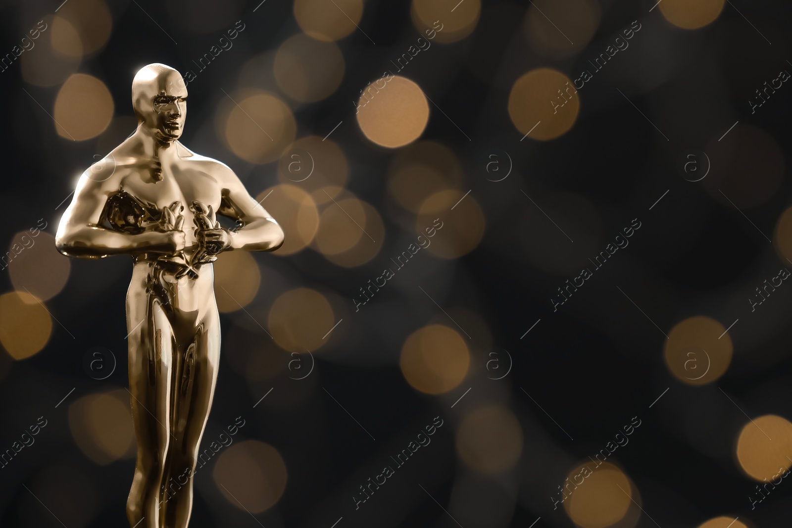 Photo of Golden trophy in shape of human figure on black background with blurred lights, space for text