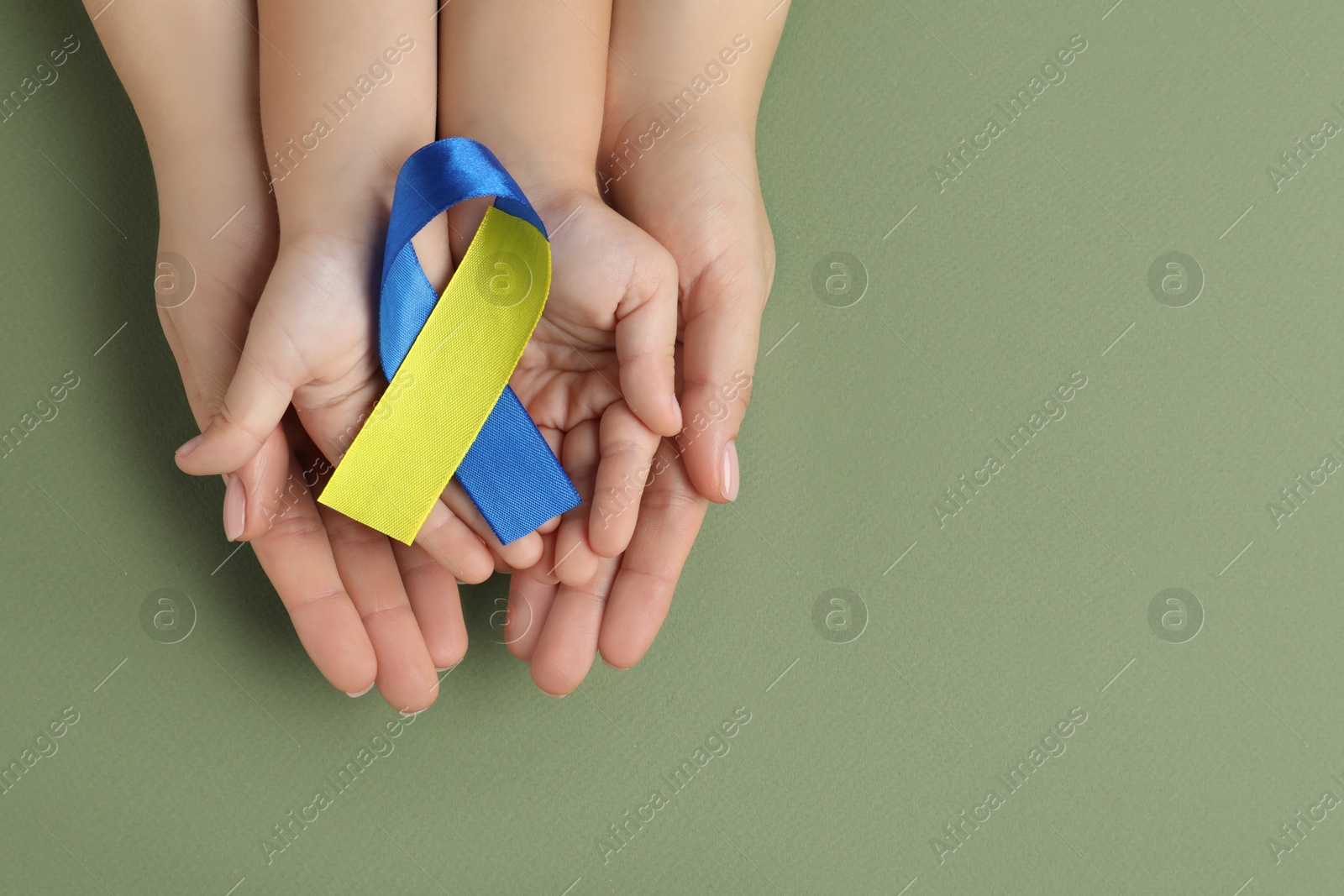 Photo of Woman with child holding yellow and blue ribbon on green background, top view. Down syndrome awareness