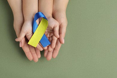 Photo of Woman with child holding yellow and blue ribbon on green background, top view. Down syndrome awareness