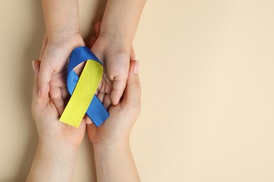 Photo of Woman with child holding yellow and blue ribbon on beige background, top view. Down syndrome awareness