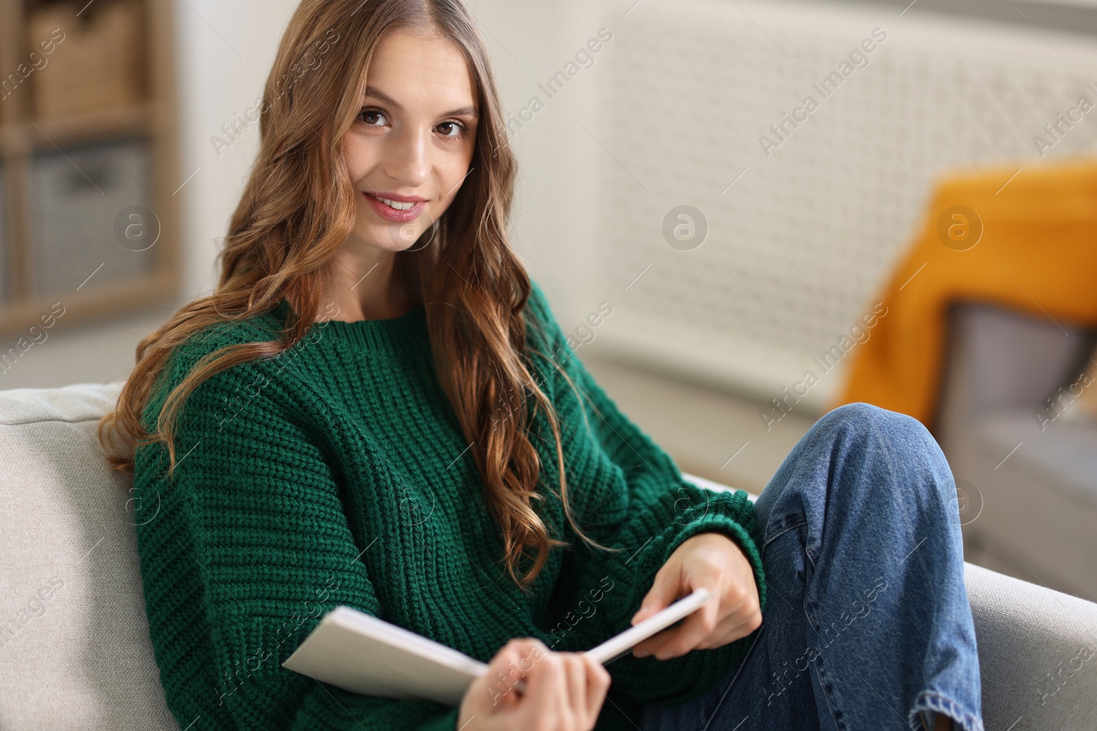 Photo of Charming young woman reading book on sofa at home. Autumn atmosphere