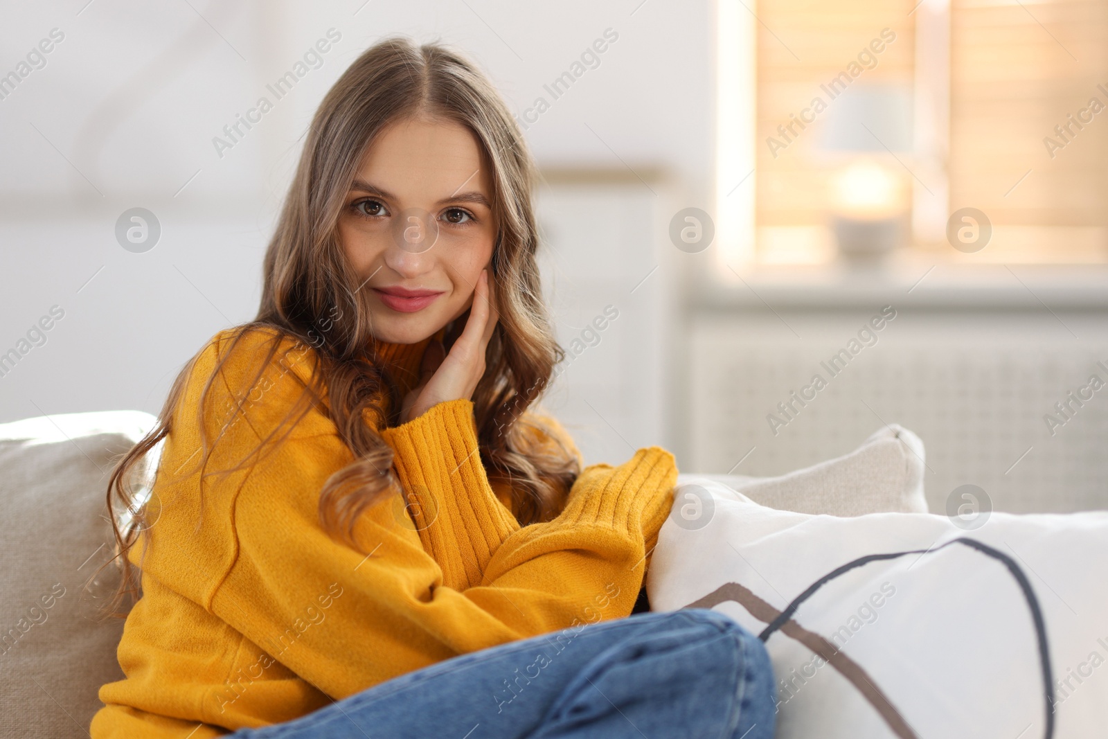 Photo of Charming young woman on sofa at home, space for text. Autumn atmosphere