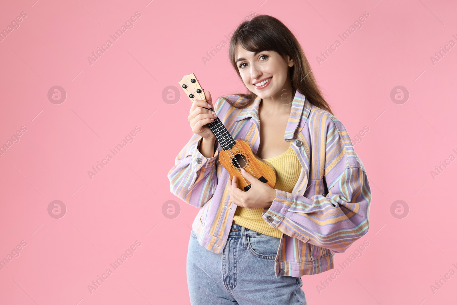 Photo of Happy woman playing ukulele on pink background, space for text