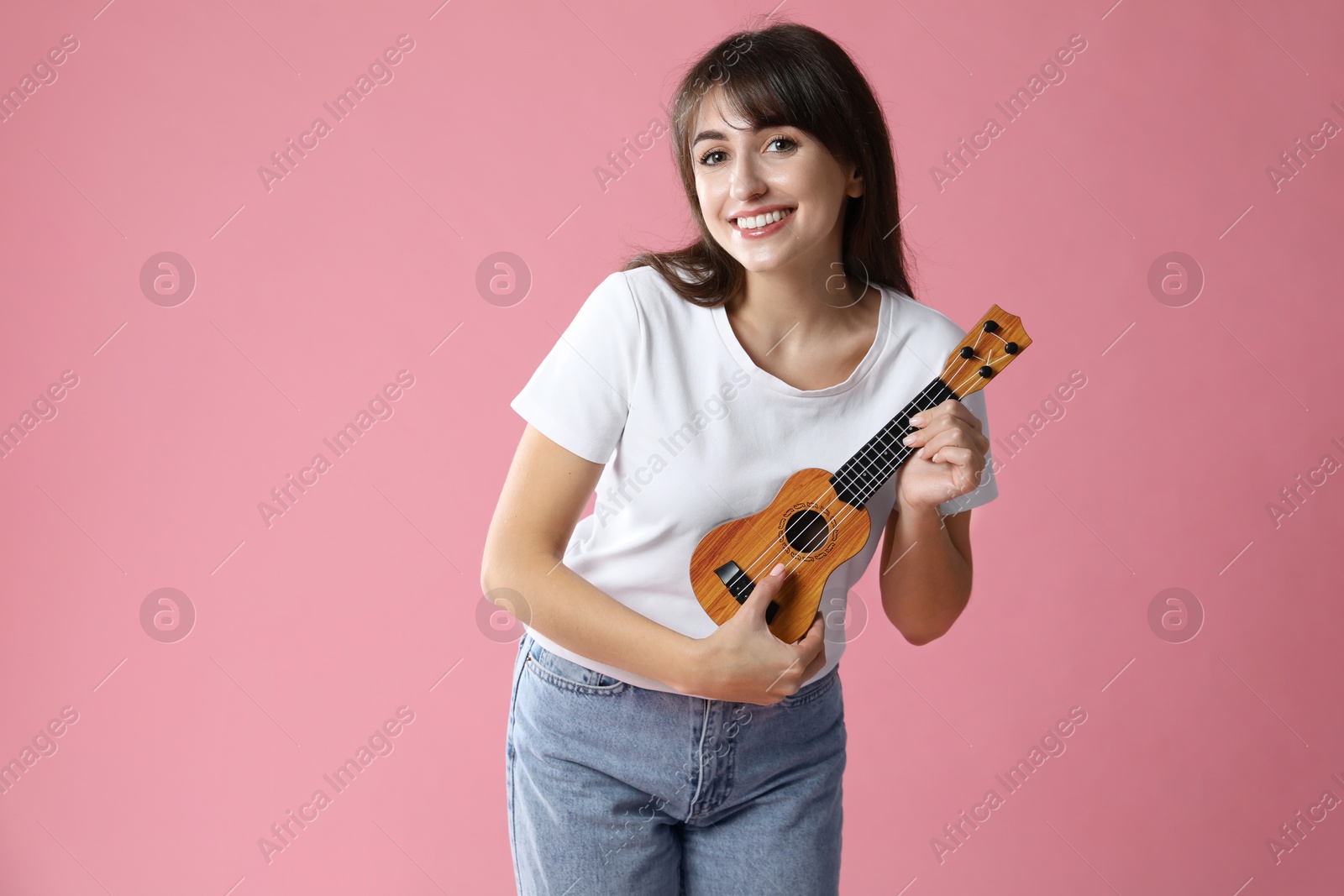 Photo of Happy woman playing ukulele on pink background