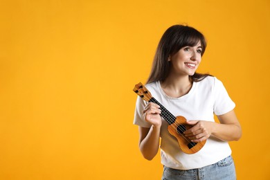 Photo of Happy woman playing ukulele on orange background, space for text