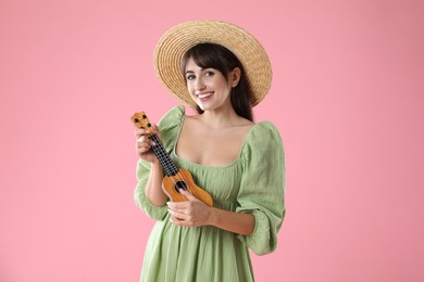 Happy woman playing ukulele on pink background