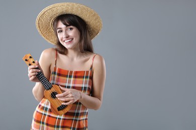 Happy woman playing ukulele on grey background, space for text