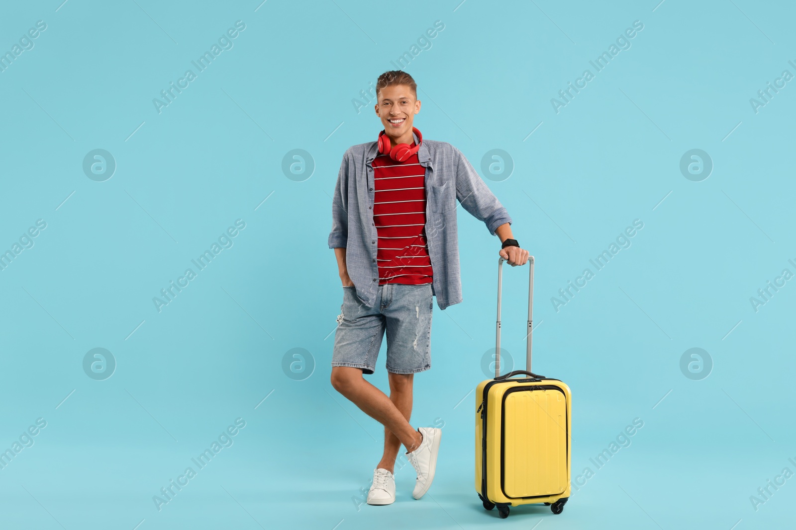 Photo of Happy traveller with suitcase on light blue background