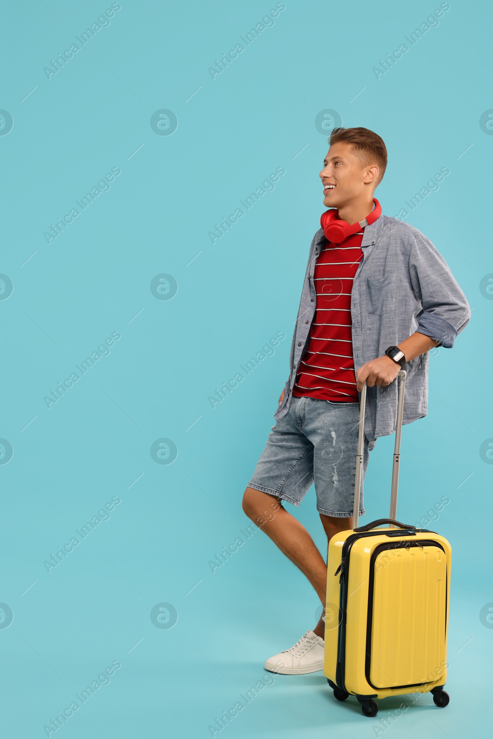 Photo of Happy traveller with suitcase on light blue background. Space for text