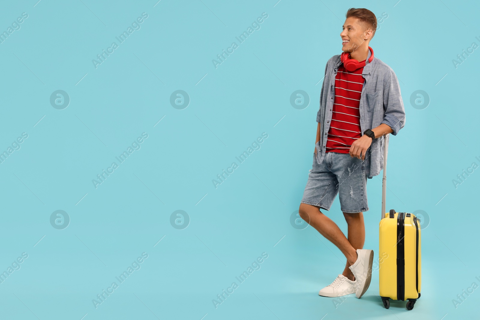 Photo of Happy traveller with suitcase on light blue background, space for text