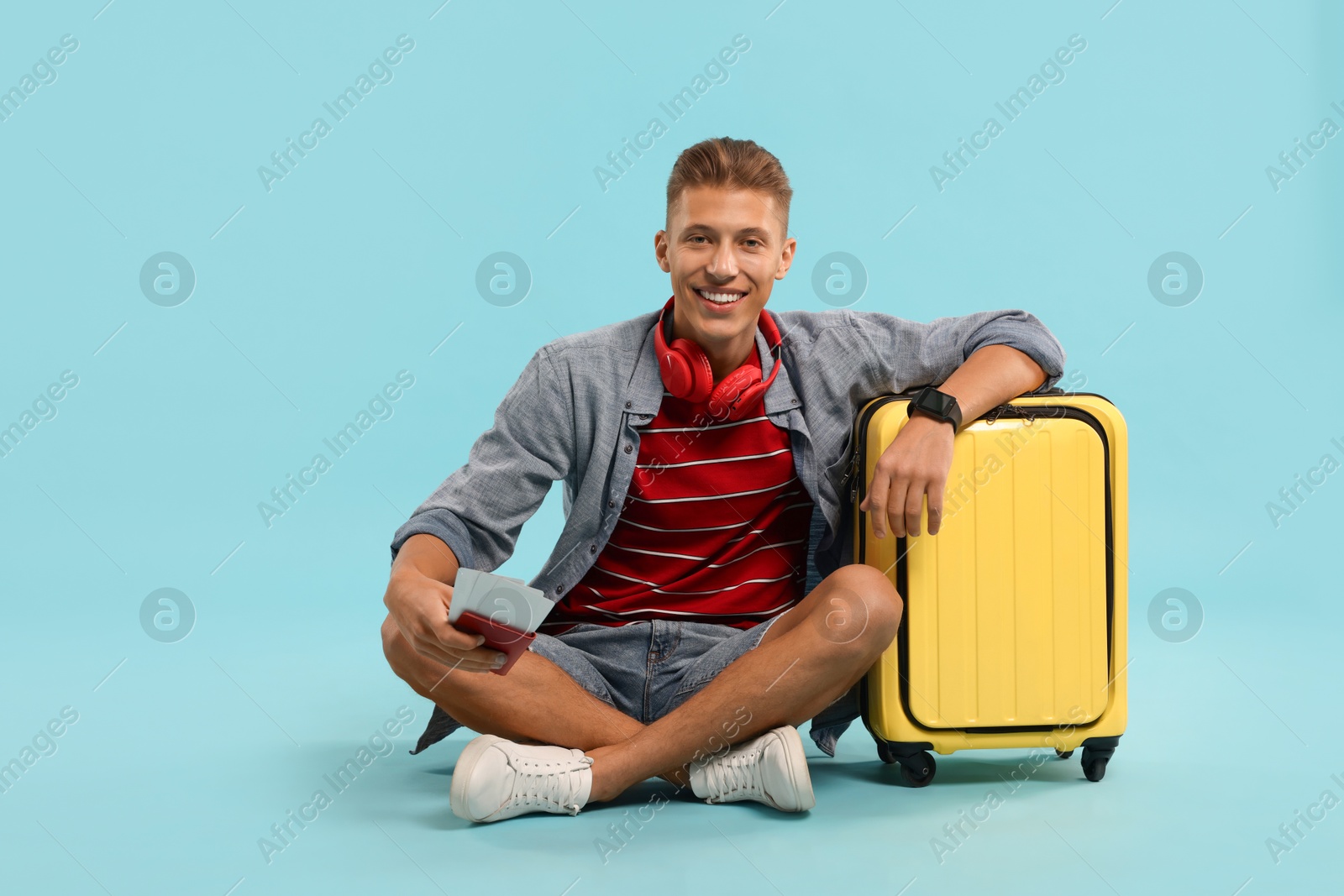 Photo of Happy traveller with suitcase, passport and ticket on light blue background