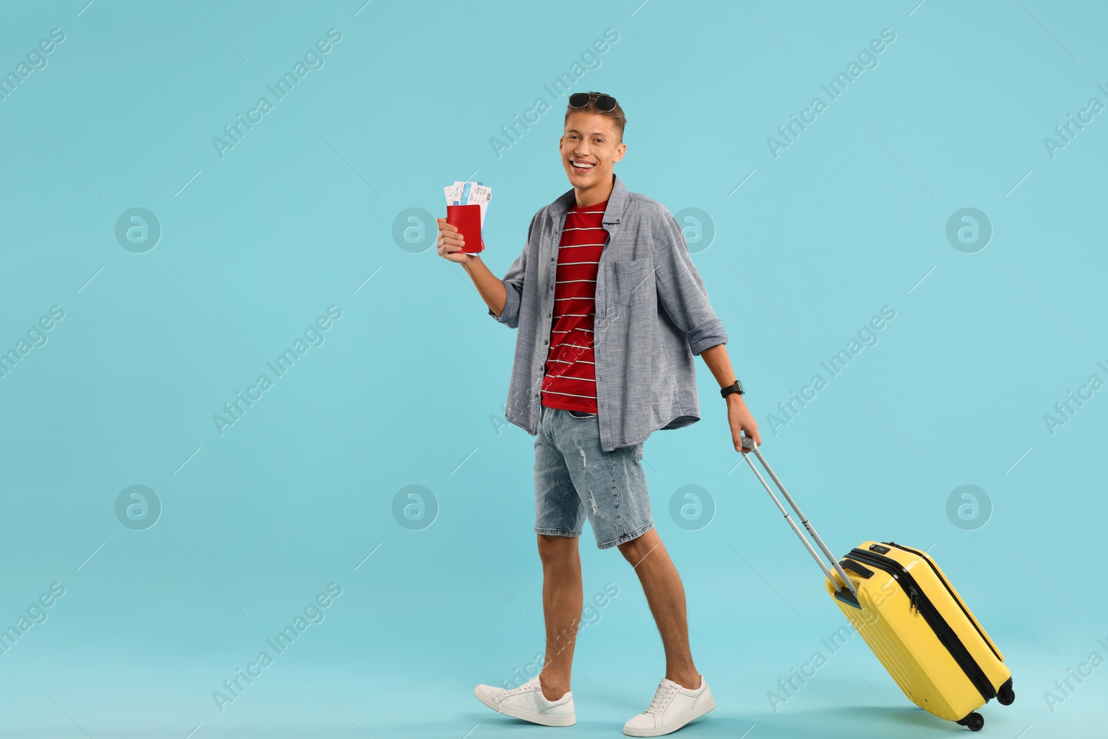 Photo of Happy traveller with suitcase, passport and tickets on light blue background