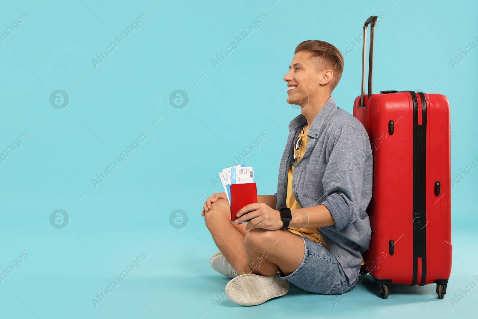 Photo of Happy traveller with suitcase, passport and tickets on light blue background, space for text