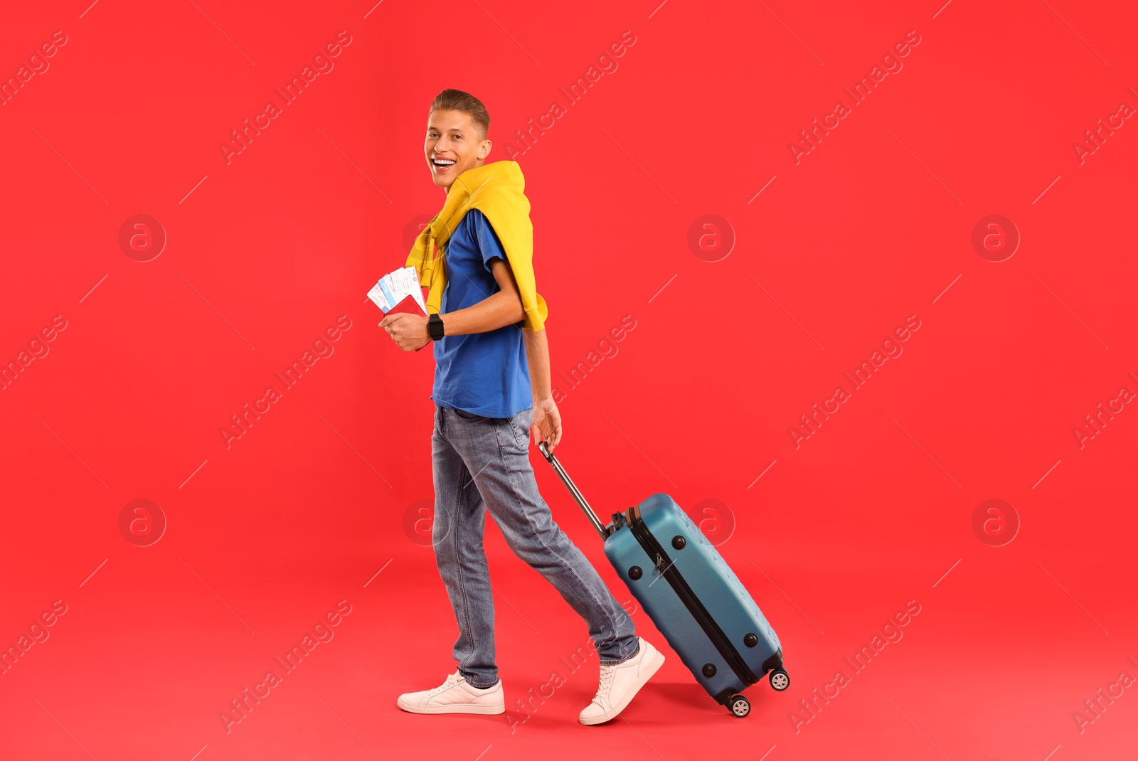 Photo of Happy traveller with suitcase, passport and tickets on red background