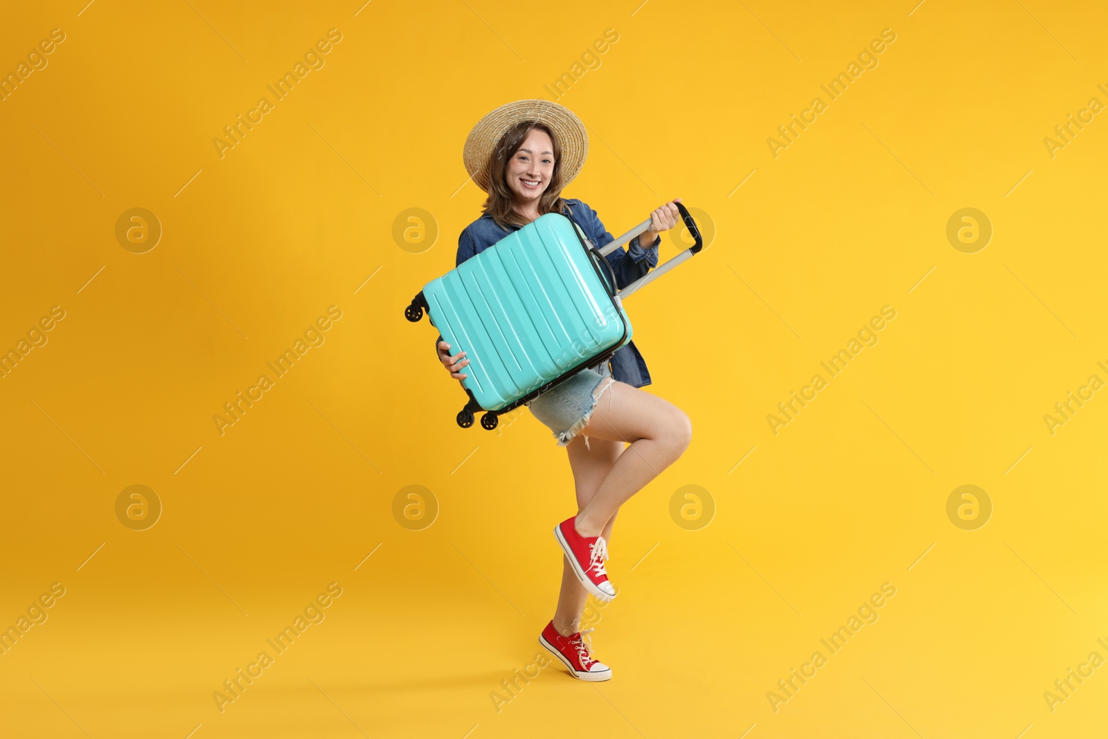 Photo of Happy traveller with suitcase on yellow background