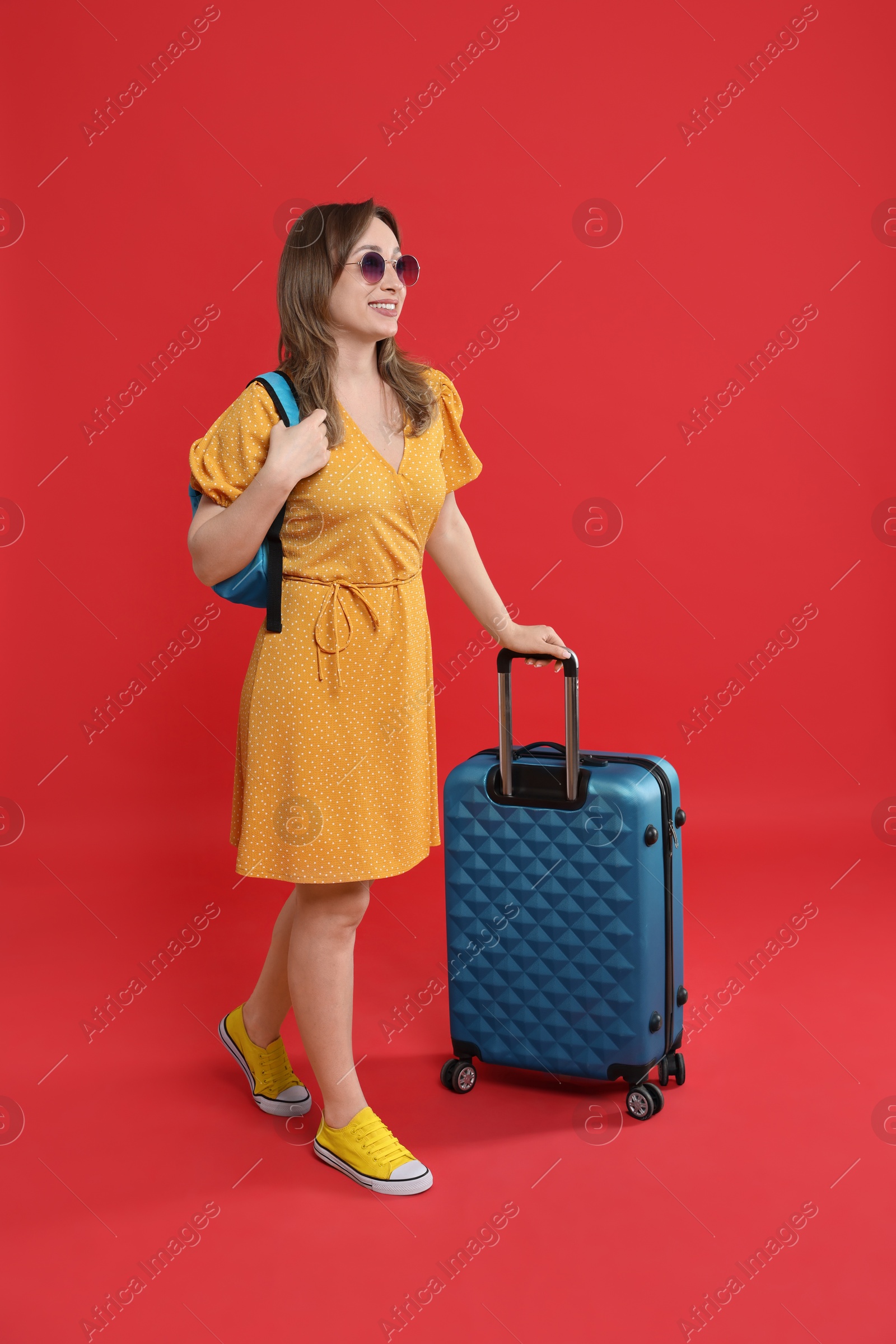 Photo of Happy traveller in sunglasses with suitcase on red background