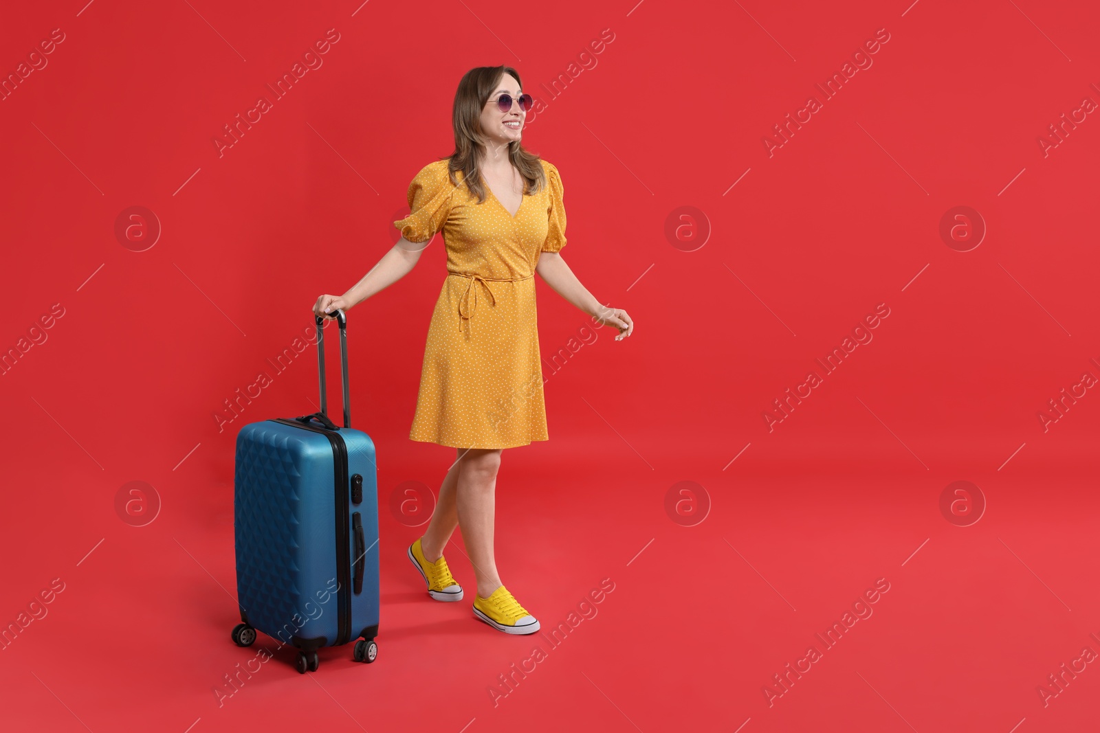 Photo of Happy traveller in sunglasses with suitcase on red background. Space for text