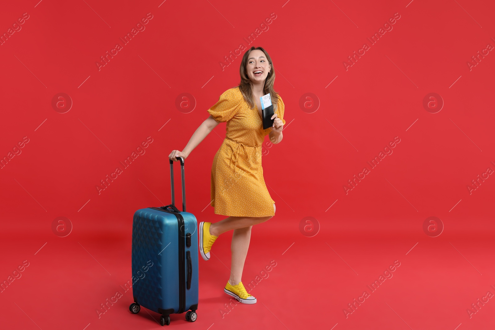 Photo of Happy traveller with suitcase, passport and ticket on red background