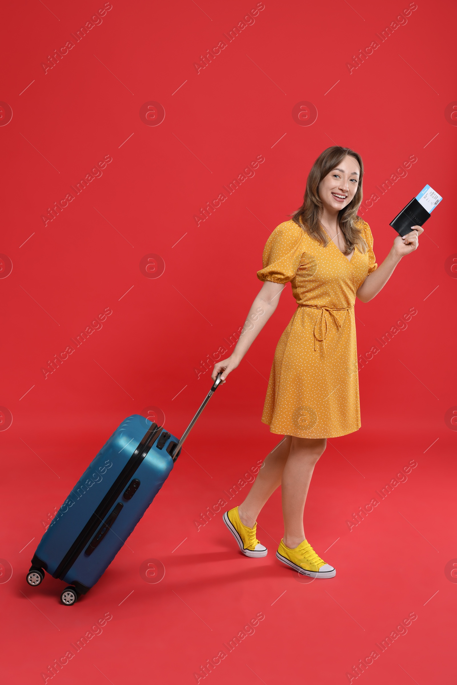 Photo of Happy traveller with suitcase, passport and ticket on red background