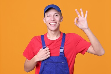 Photo of Happy young man in uniform showing OK gesture on orange background