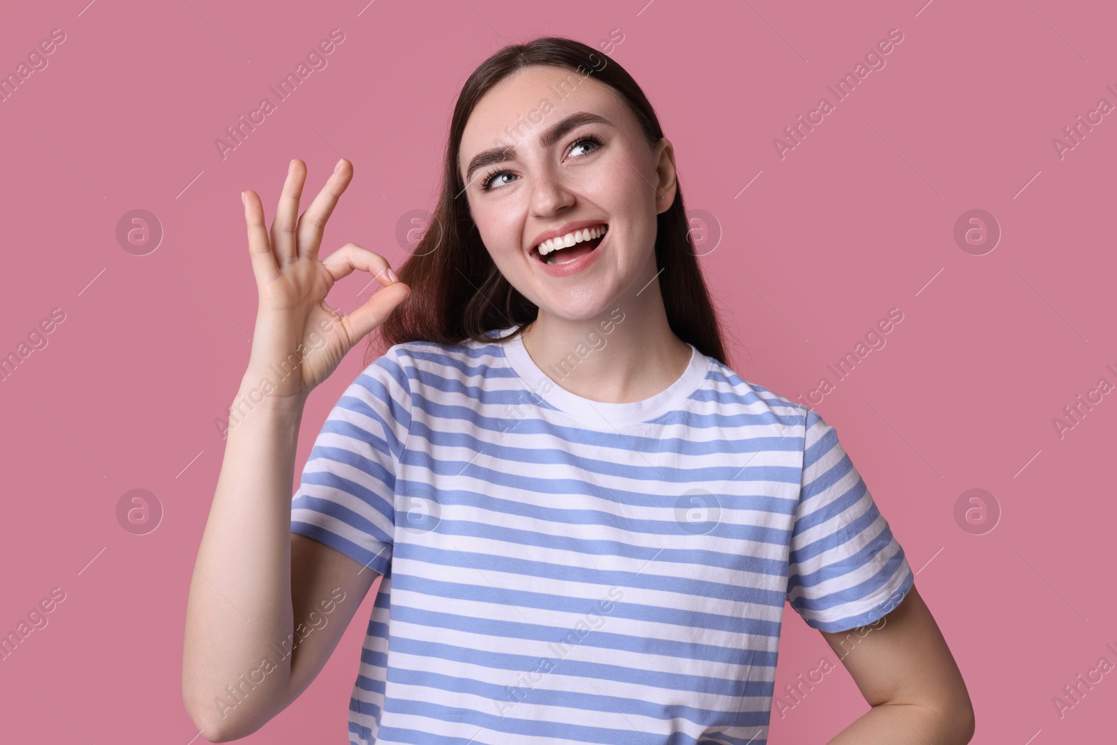 Photo of Happy young woman showing OK gesture on pink background